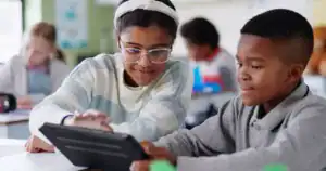 Dupla de alunos interagindo colaborativamente com um tablet em sala de aula, ilustrando a união entre tecnologia e desenvolvimento humano na Educação 5.0.